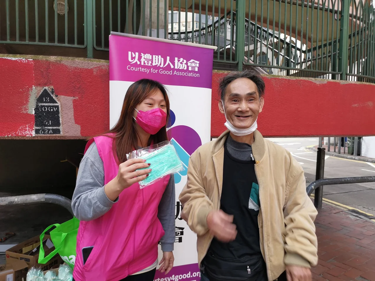 義工在街頭派發口罩,與參與者交流及合照;場地可見以禮助人協會易拉架。